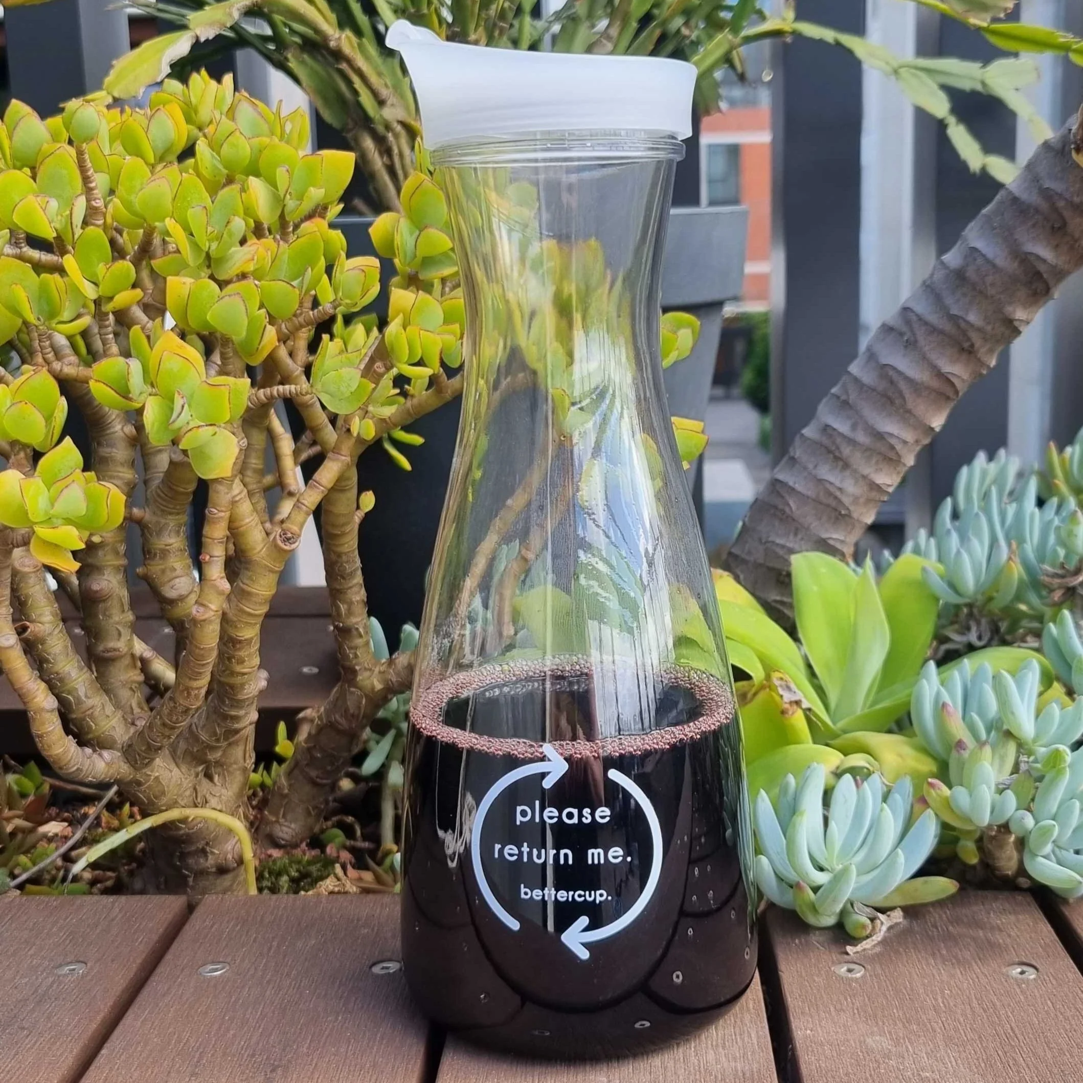 Plastic wine carafe filled with red wine, with the custom printed text "please return me" and Bettercup printed on the front.
