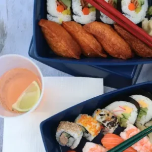 Reusable black betterdish with sushi, rice and fried chicken being served at an event.