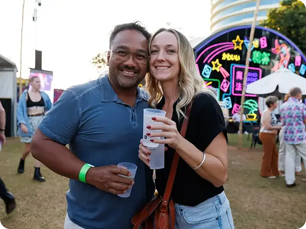 Three reusable cups with bettercup custom printed brandingheld by a man and a woman at a festival in Australia.