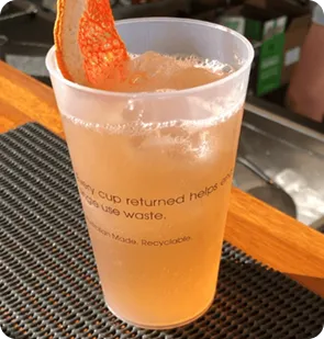 A close-up photo of a bettercup tumbler with an orange drink and a citrus garnish on a bar counter.