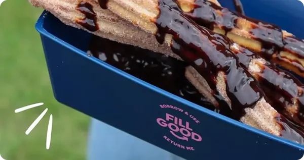 A person holding a FillGood betterdish filled with churros drizzled with chocolate sauce.