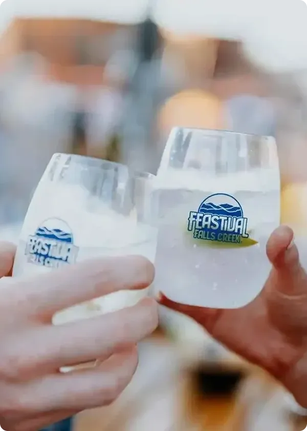 Two people holding glasses in a toast at Eastvail Falls Creek, with blurred background of a building and outdoor setting.