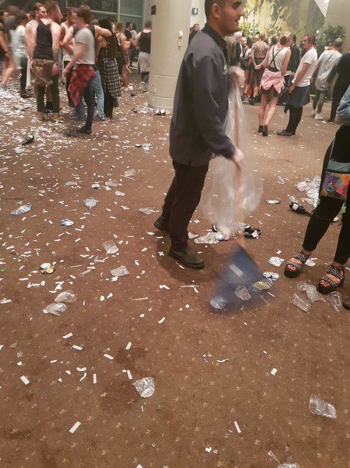 Plastic cups and waste littered on the ground at an event with people walking through.